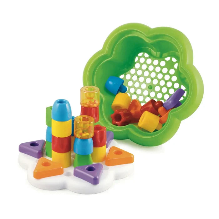 Colorful chunky pegs in various shapes stacked on a white base next to a green flower-shaped storage bowl.