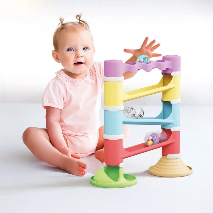 Baby girl playing with a four-tier pastel marble run tower and clear balls filled with colorful rattling beads.