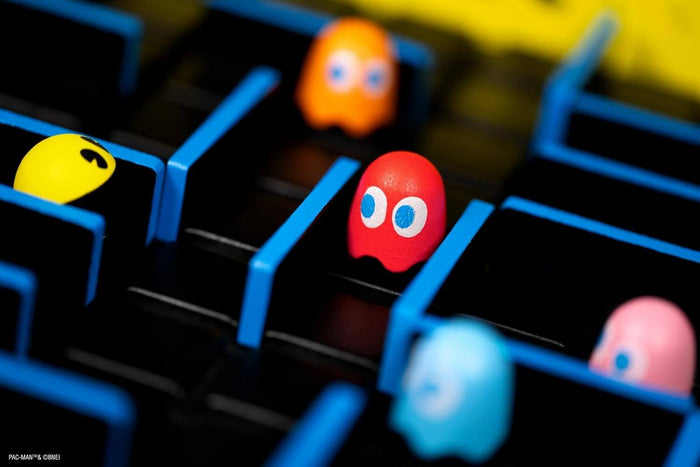 Close-up of yellow Pac-Man and colorful ghost figurines inside a maze of blue walls on a black board.