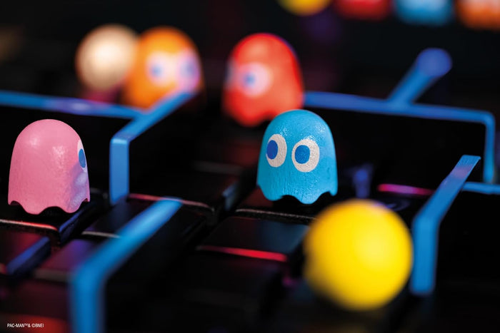 Close-up of wooden pink, blue, red, and orange ghost figures and a yellow Pac-Man figure on a black and blue maze board.