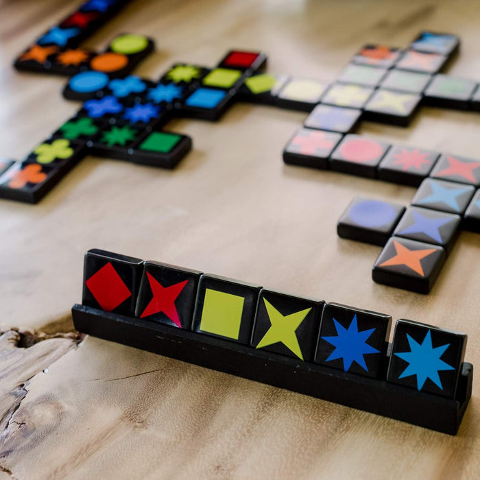 Close-up of black game tiles with vibrant colored shapes like stars and squares on a wooden tray and table.