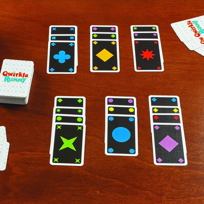 Qwirkle Rummy card game with colorful geometric shapes on black cards arranged in sets on a dark wood table.