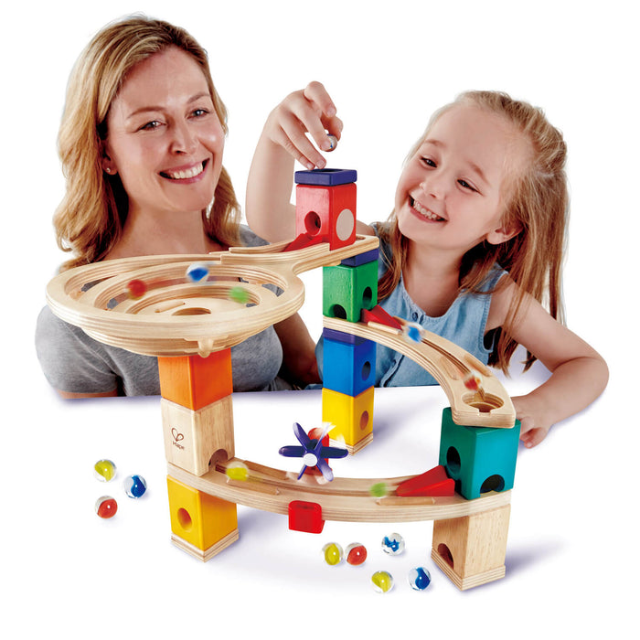 Woman and child play with a tiered wooden toy with colorful blocks, a spiral funnel, and glass marbles.