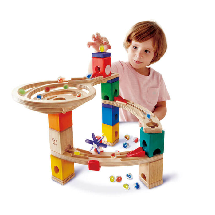Child playing with a wooden marble run made of colorful blocks, curved tracks, and a spiral bowl.
