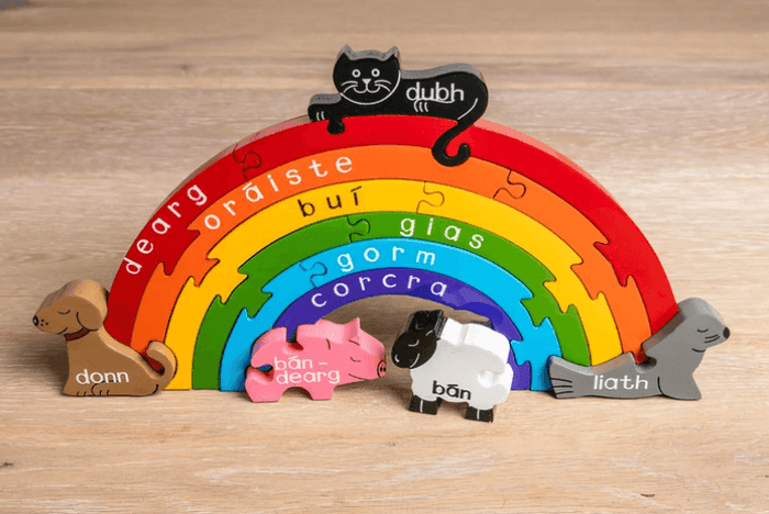 Wooden rainbow puzzle with Irish color names and animal-shaped pieces including a cat, dog, pig, sheep, and seal.