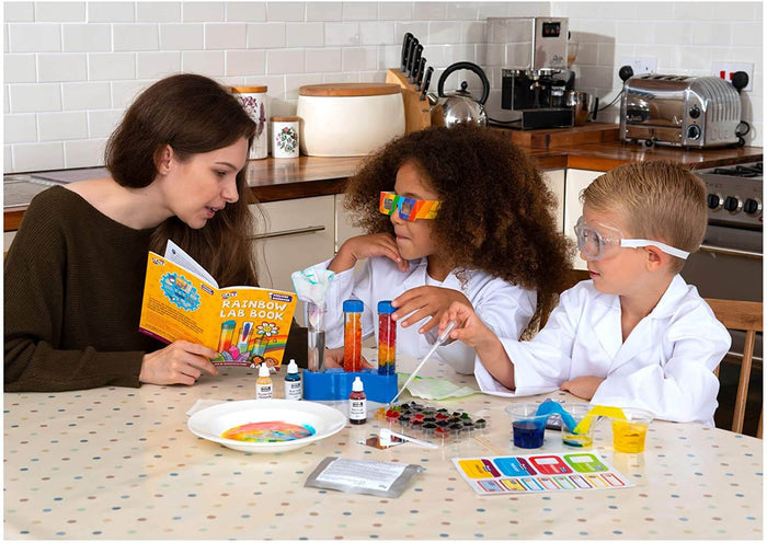 A woman and two children in lab coats experiment with colorful liquids, test tubes, and a rainbow lab book.