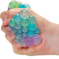 Hand squeezing a multi-colored squishy toy, creating clusters of translucent green, blue, and purple bubbles.