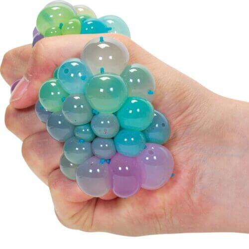 Hand squeezing a multi-colored squishy toy, creating clusters of translucent green, blue, and purple bubbles.