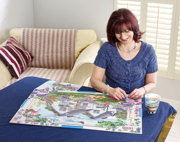 A woman completes a puzzle on a white board with blue side clips, resting on a blue tablecloth.
