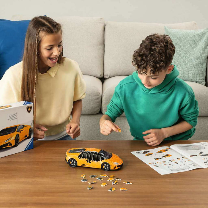 Two children assembling an orange 3D supercar puzzle at a table with loose pieces, instructions, and product box.