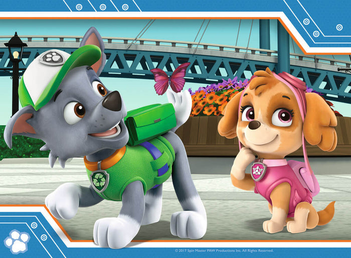 Grey pup Rocky and tan pup Skye smile at a pink butterfly on Rocky's tail in front of a blue bridge and flowers.