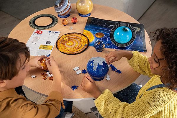 Two children building colorful 3D spherical planet puzzles on a round table with a solar system poster and instructions.