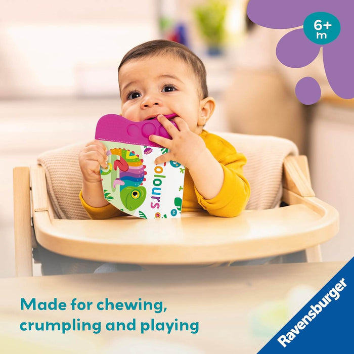 Baby in a high chair chewing on the purple teether top of a soft book with a colorful chameleon.