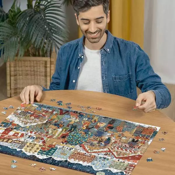 Man assembling a colorful, snowy Christmas market jigsaw puzzle on a wooden table with scattered pieces.