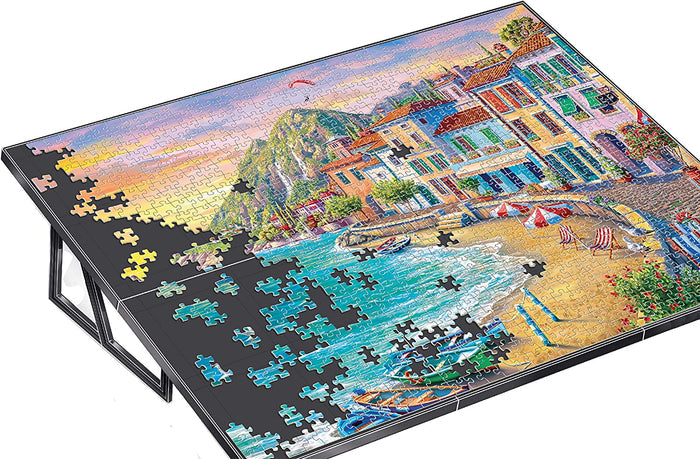 Black tilted puzzle board easel holding a partially completed jigsaw puzzle of a colorful seaside village.