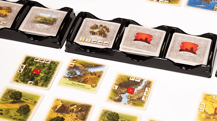 Close-up of a board game setup showing black plastic card holders with illustrated cards, plus several scattered landscape and resource cards on a white surface.