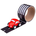 Black tape roll with white road markings and a crosswalk, featuring a small red toy car on the unrolled strip.