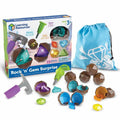 Toy geode set with hammer, chisel, blue bag, and brown plastic rocks cracking open to reveal colorful faceted gems.