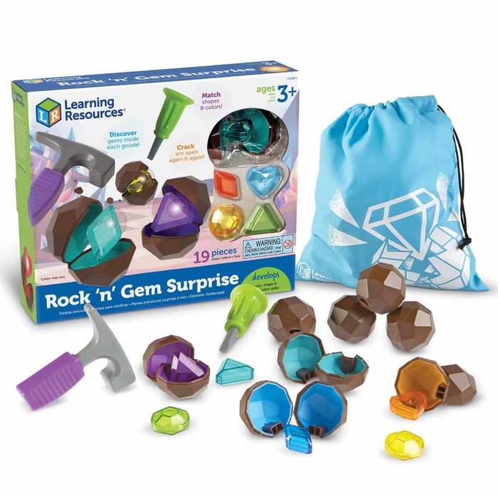 Toy geode set with hammer, chisel, blue bag, and brown plastic rocks cracking open to reveal colorful faceted gems.