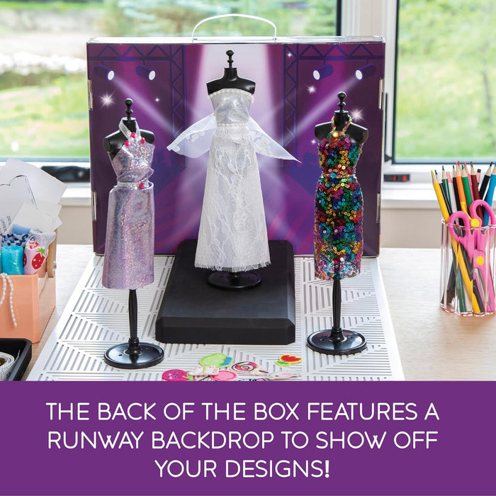 Three mannequins in sparkly purple, white lace, and sequined dresses on a runway backdrop with art supplies.