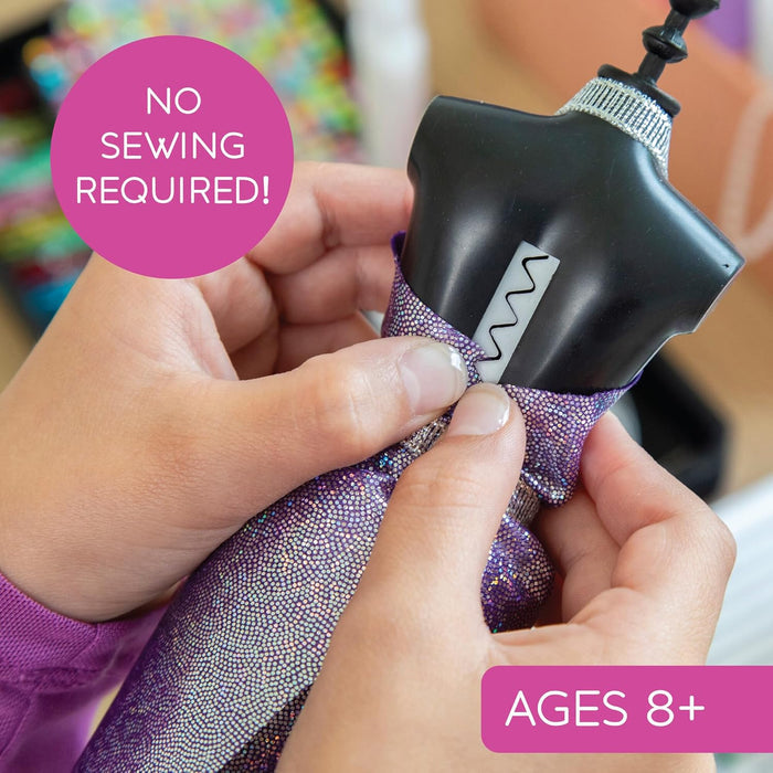 Hands fitting purple glitter fabric onto a black dress form's zigzag slot. Text: No Sewing Required and Ages 8+.
