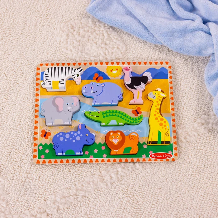 Wooden puzzle with 8 colorful chunky safari animals on a scenic board, set on a white shaggy rug and blue blanket.