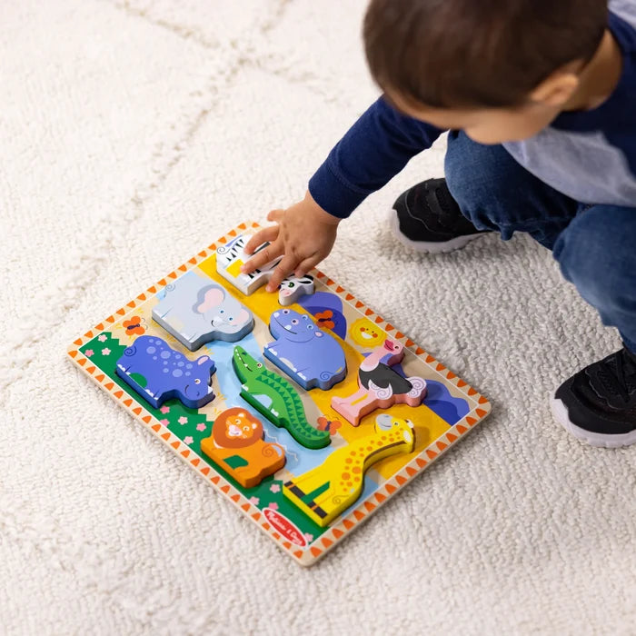 Child placing a zebra piece into a colorful wooden safari puzzle with chunky animal shapes on a white rug.