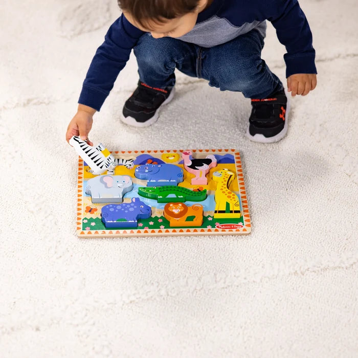 Child holding a chunky wooden zebra piece over a colorful safari puzzle with a lion, elephant, and giraffe.