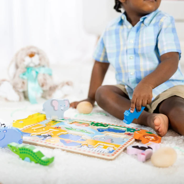 Child playing with chunky wooden animal pieces and a colorful safari-themed board puzzle on a white fuzzy rug.