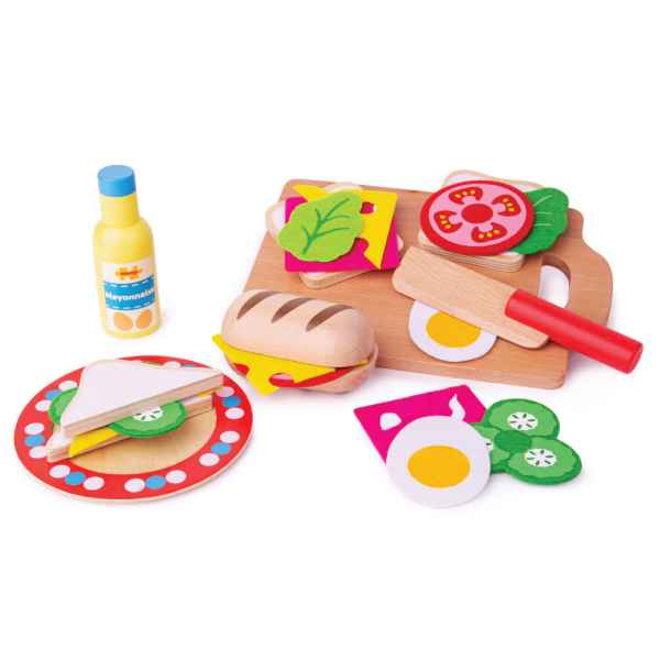 Wooden toy sandwich set with colorful bread, veggies, cutting board, red-handled knife, plate, and mayonnaise bottle.