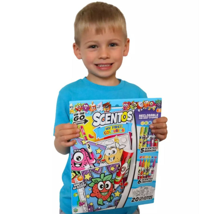Smiling boy holding a colorful Scentos activity pack featuring cartoon characters, markers, and crayons.