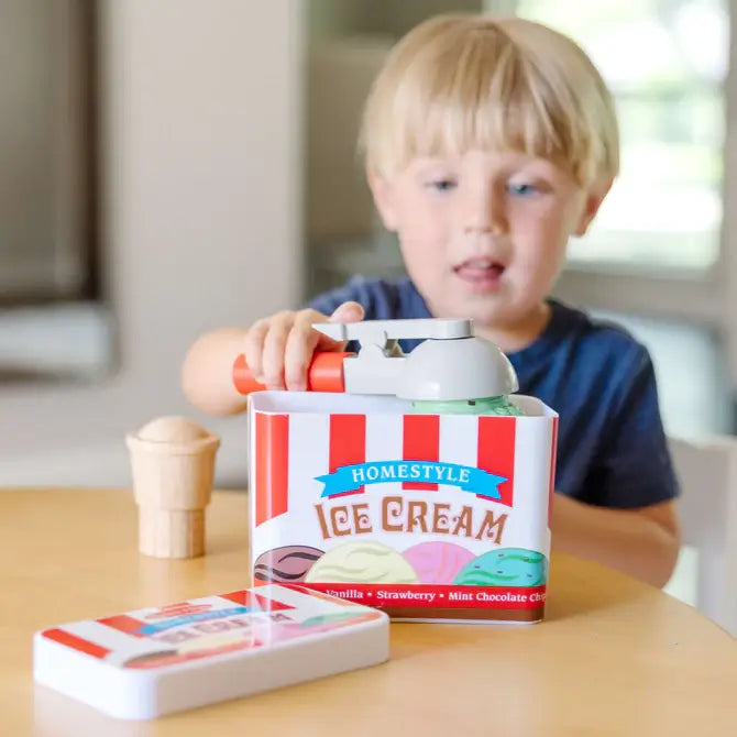 A child uses a magnetic scooper to lift a green scoop from a red and white striped toy ice cream tub.