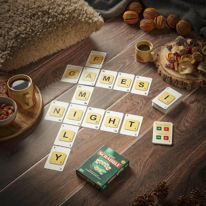 Scrabble cards spelling Family Night Games on a wooden table next to the green box, coffee mugs, and snacks.