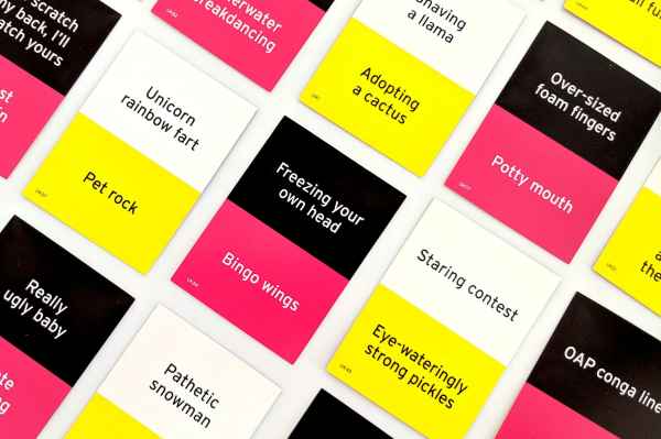 Colorful party game cards in pink, yellow, white, and black with funny phrases like Pet rock and Bingo wings.