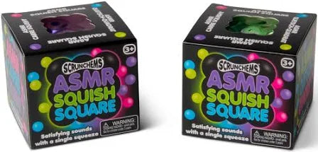 Two black cube boxes with neon graphics and top windows revealing purple and green squishy square toys.
