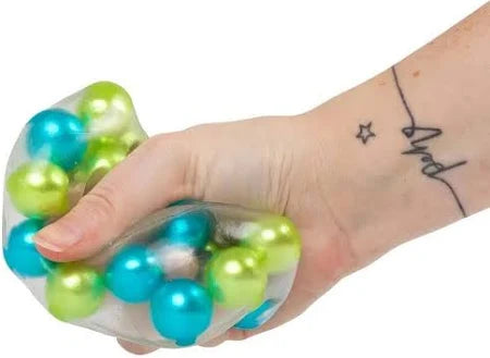 Hand squeezing a clear squishy square toy filled with metallic blue and green beads.