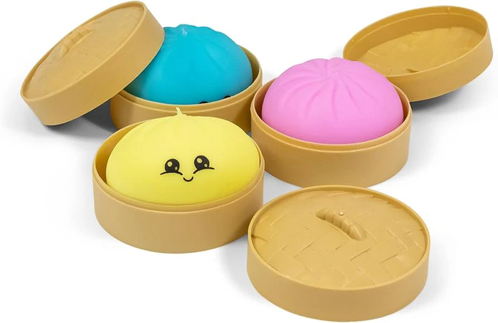 Blue, pink, and yellow squishy toy dumplings in tan plastic steamer baskets; the yellow dumpling has a smiling face.