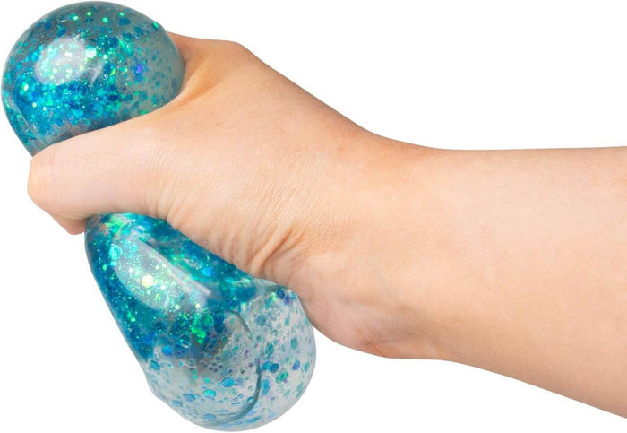 Hand squeezing a translucent squishy toy filled with vibrant blue and green hexagonal glitter and sparkles.