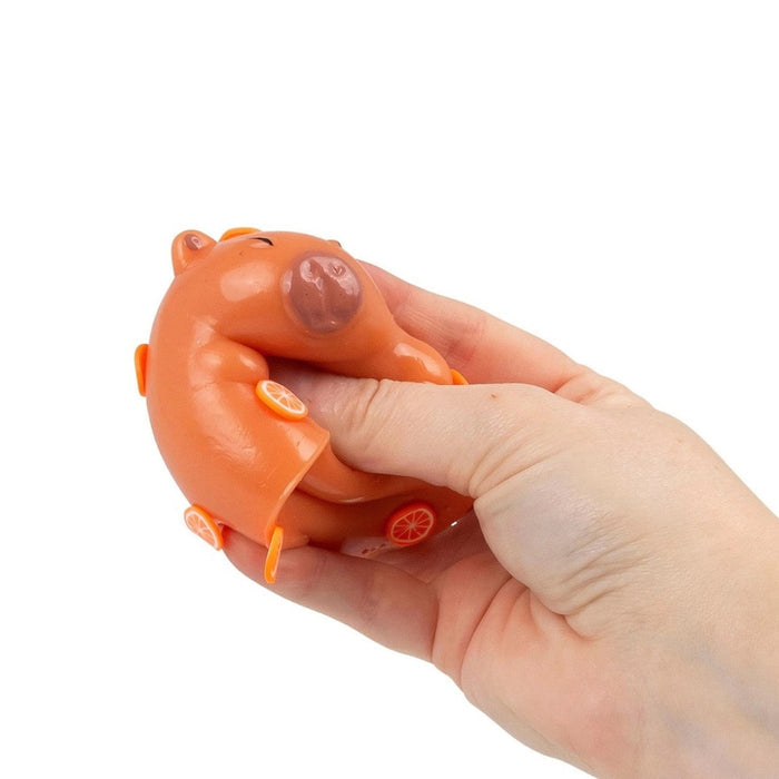 A person's hand squeezes an orange capybara-shaped squishy toy decorated with small orange slice details.