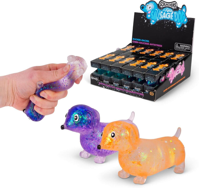 Hand squeezing a glittery purple squishy dog beside standing orange and purple toys and a product display box.