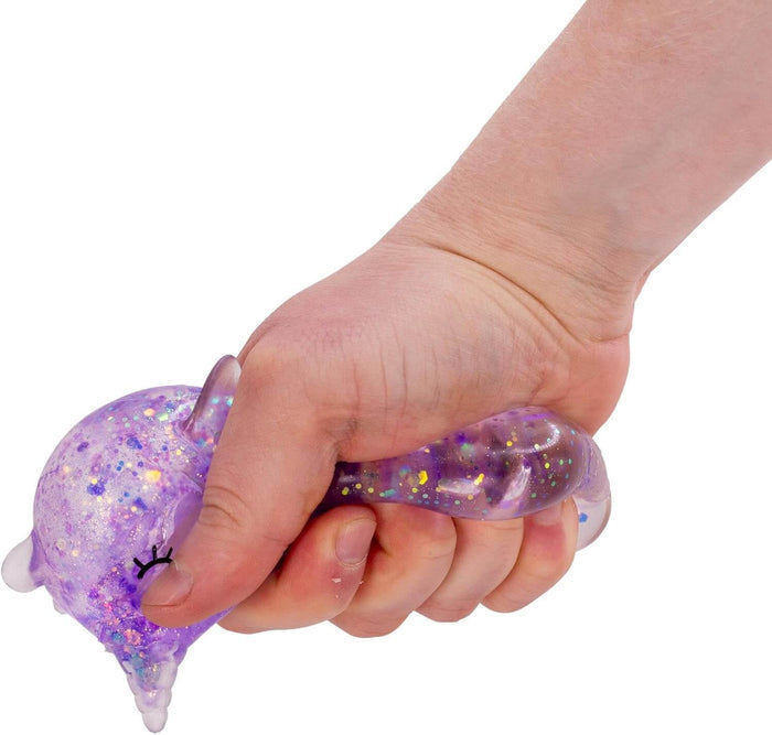 Hand squeezing a purple translucent narwhal-shaped squishy toy filled with sparkling glitter and stars.