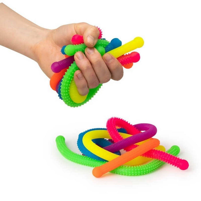 Hand squeezing colorful, bumpy, flexible noodles with more textured toys piled on a white background.