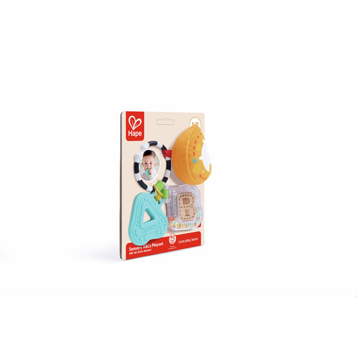 Packaged Hape baby toy set with teal A teether, striped mirror rattle, yellow plush, and clear B rattle with beads.