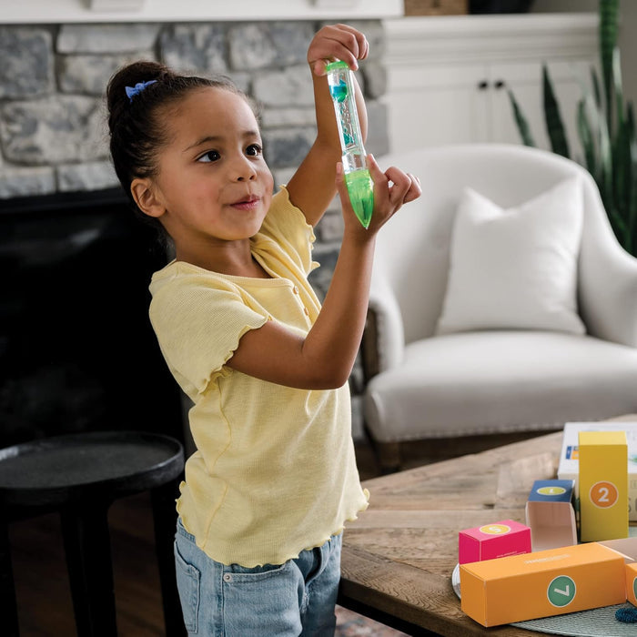 Young girl playing with a green liquid motion bubbler next to colorful numbered advent calendar boxes.