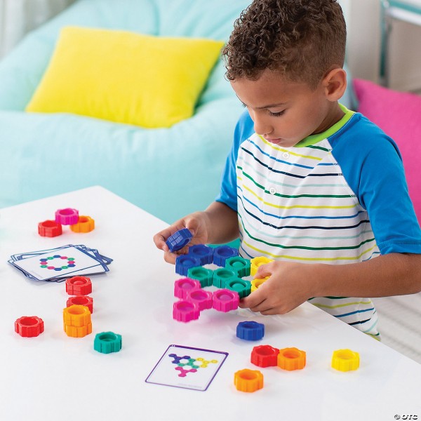 Boy connecting colorful hexagonal popping toys to match patterns on design cards at a white table.