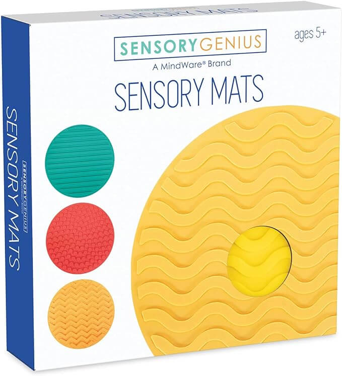 White box showing teal, red, and orange textured circular mats alongside a large yellow wavy mat for sensory play.