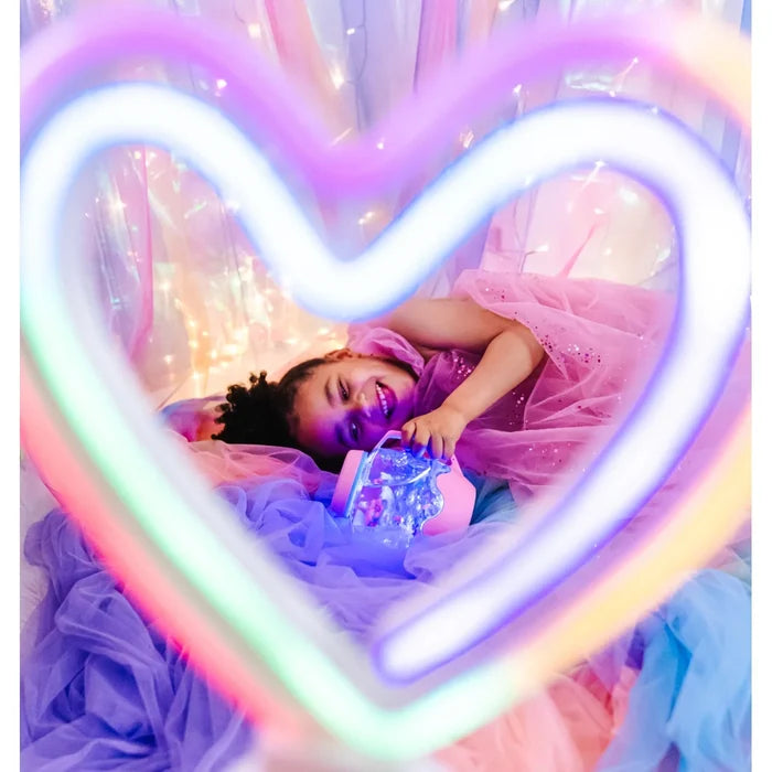Young girl holds a pink jar with glitter inside, framed by a colorful neon heart and pastel tulle.