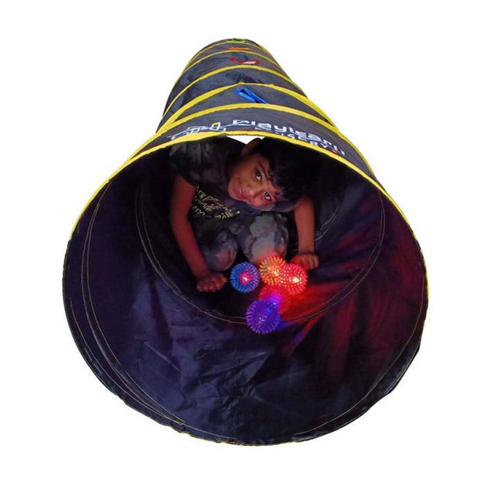 Child inside a long black tunnel with yellow stripes playing with glowing red, blue, and purple sensory balls.