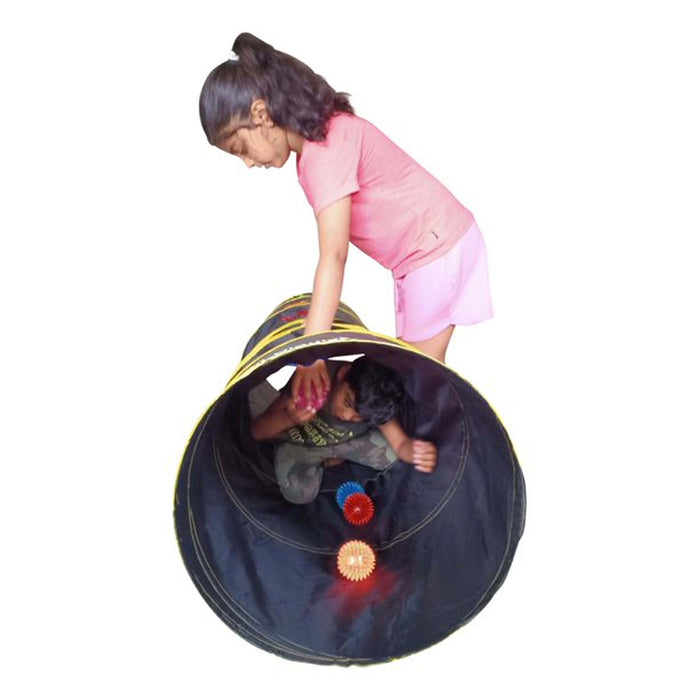 A girl looks into a black sensory tunnel as a boy crawls through with glowing red and blue LED spiky balls.