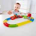 Toddler playing with a colorful wooden train set featuring a musical bridge and sensory blocks on an oval track.